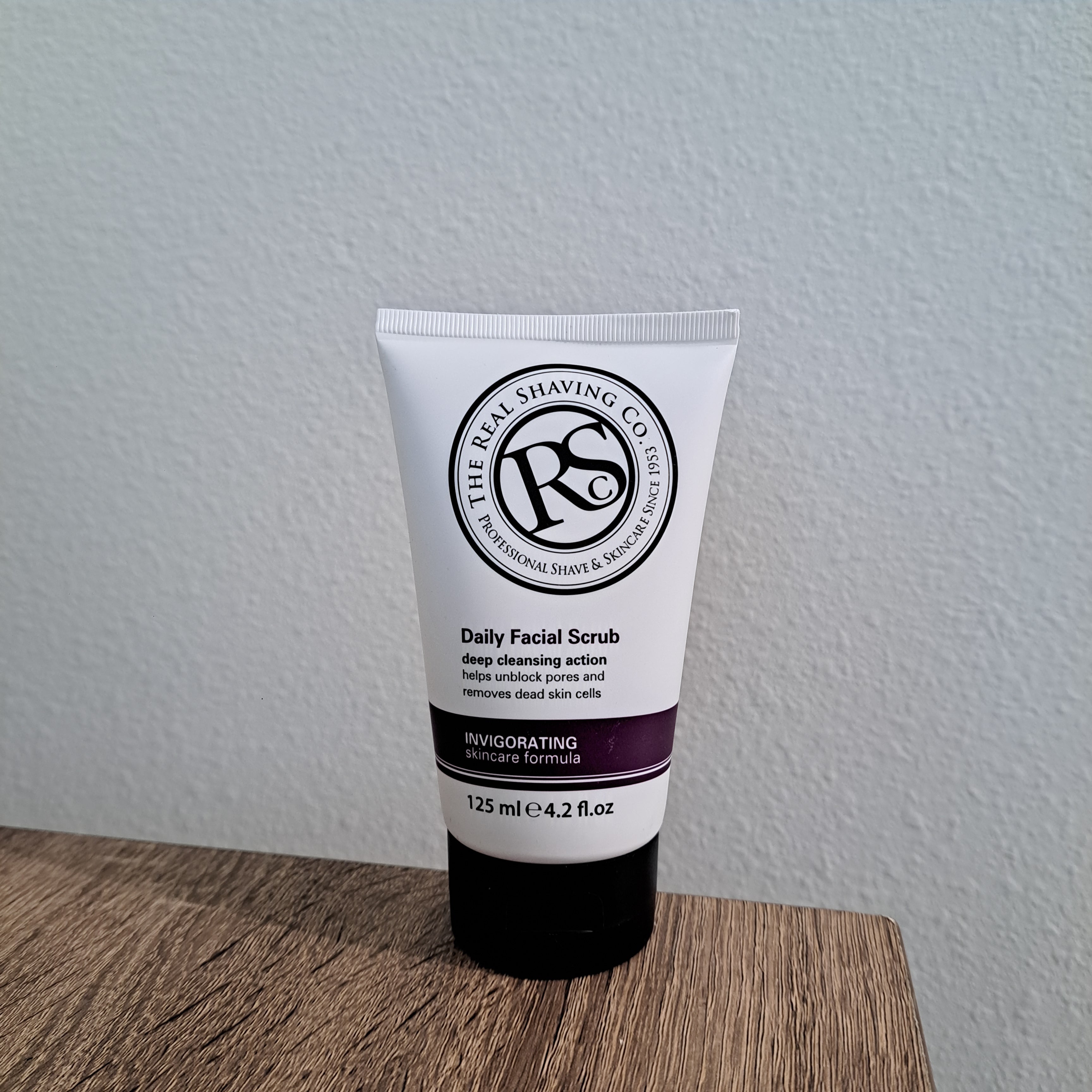 Tube of Daily Facial Scrub on a white surface with a wooden edge
