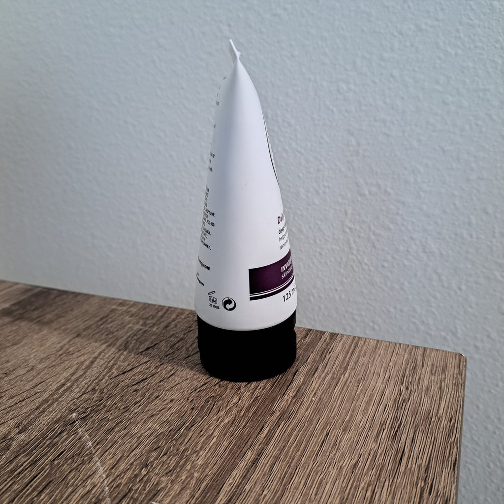White tube with a black cap on a wooden surface against a light gray wall
