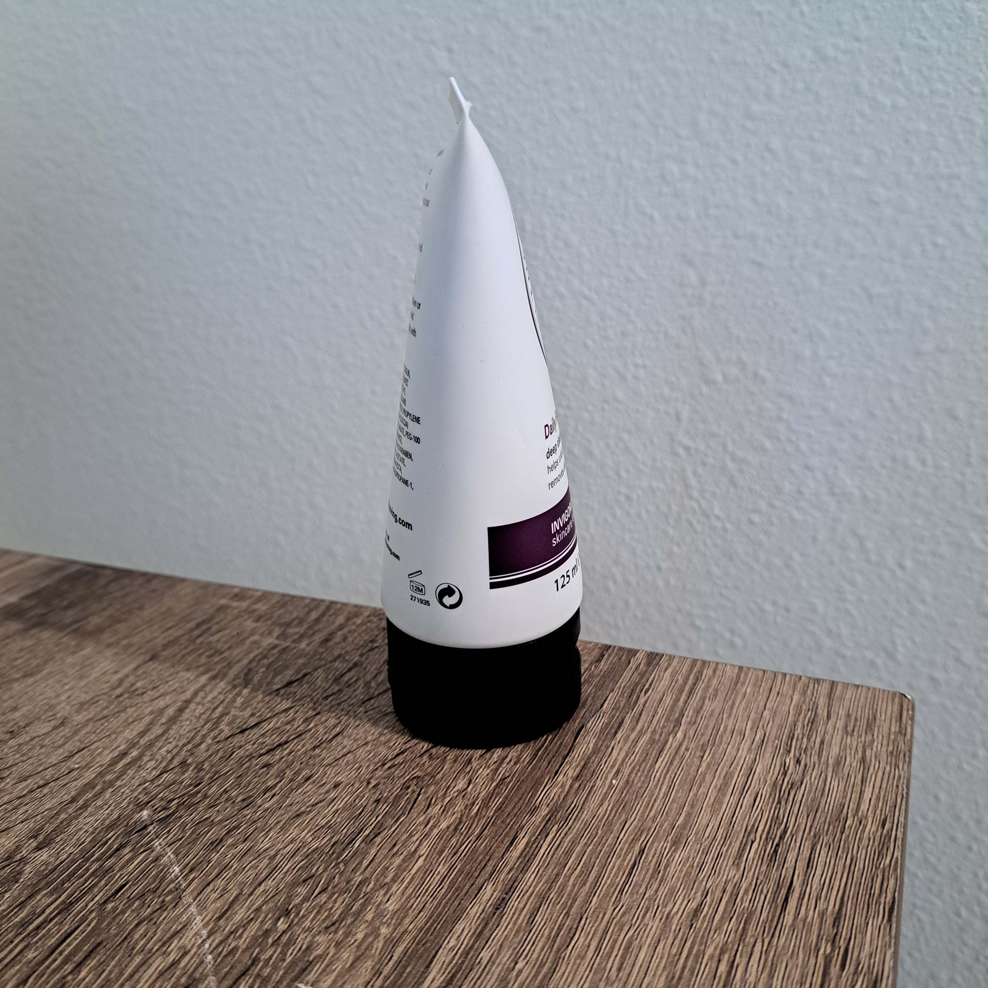 White tube with a black cap on a wooden surface against a light gray wall